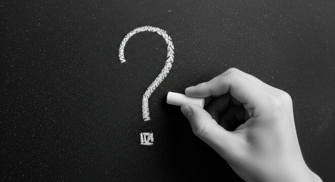 Hand writing question mark on chalkboard with chalk, monochrome image