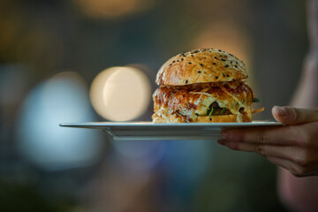 Gourmet burger served on plate in warm natural light with soft bokeh background. Ideal for: restaurant marketing, food delivery, menu design, gastronomy, lifestyle content. Colours: brown, gold, beige