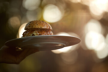 Gourmet burger served on plate in warm natural light with soft bokeh background. Ideal for: restaurant marketing, food delivery, menu design, gastronomy, lifestyle content. Colours: brown, gold, beige