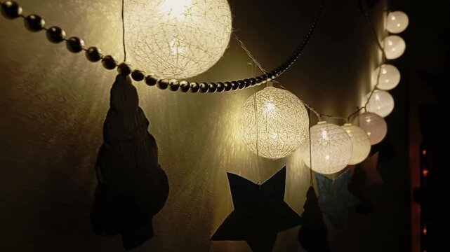A string of round light bulbs. The garland hangs among beads and figures. The garland is made of round balls with soft white light.