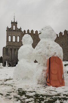 A lively winter scene at the northern stone fortifications of Avila, Spain, where locals and visitors play in the deep snow and build snowmen against the backdrop of the historic medieval walls.