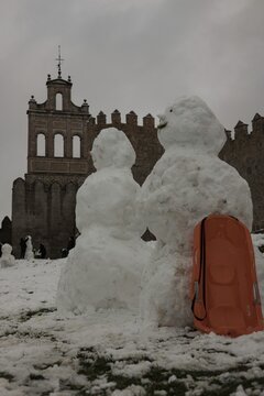 A lively winter scene at the northern stone fortifications of Avila, Spain, where locals and visitors play in the deep snow and build snowmen against the backdrop of the historic medieval walls.