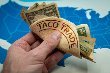 Hand holding a taco shell labeled TACO TRADE. Wall Street slang for a pattern where investors buy assets after President threatens tariffs, expecting him to back down and markets to rebound © tanaonte