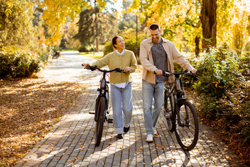 Obraz premium Korean woman and Caucasian man enjoy a sunny day walking their bikes through a colorful park