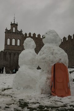 A lively winter scene at the northern stone fortifications of Avila, Spain, where locals and visitors play in the deep snow and build snowmen against the backdrop of the historic medieval walls.
