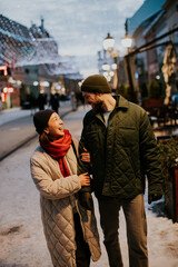 Korean woman and Caucasian man walk together on a snowy street in the evening