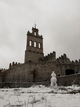  A snowman built in front of the historic Arco del Carmen gateway and the medieval stone rampart walls of Avila, Castile and Leon, Spain, during a cold and snowy winter day.