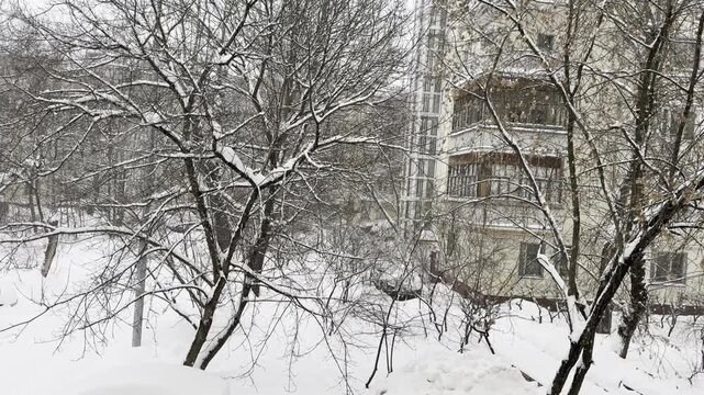 Heavy snowfall and a strong blizzard sweep between buildings in the constructivist style. Snow fills the air, reducing visibility and creating a dramatic urban winter scene with strict geometric archi