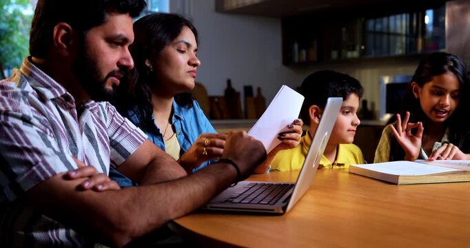 Indian young couple managing finance while kids reads book at modern home as parents work on laptop and financial documents while son and daughter study together showing family money planning