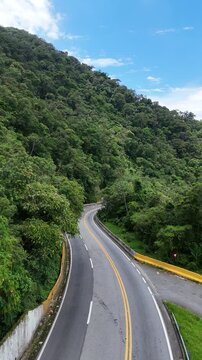 Vis&atilde;o a&eacute;rea de rodovia sinuosa atravessando as montanhas cobertas por vegeta&ccedil;&atilde;o densa, conectando o interior ao litoral paulista em meio &agrave; paisagem natural.