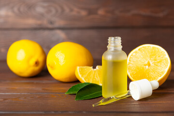 Lemon essential oil in a bottle with sliced ​​lemon and leaves on a wooden background. Lemon...