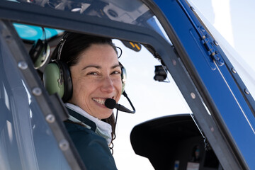 Smiling female helicopter pilot wearing a headset in the cockpit, ready for adventure © .shock