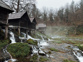 Traditional wooden watermills in Jajce, Bosnia, standing along a fast flowing stream surrounded by forest, capturing rural heritage, natural energy and historic Balkan craftsmanship.