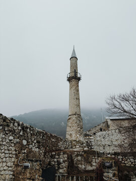 Tall stone minaret standing inside the walls of Travnik Fortress, surrounded by weathered stone and misty mountain landscape.