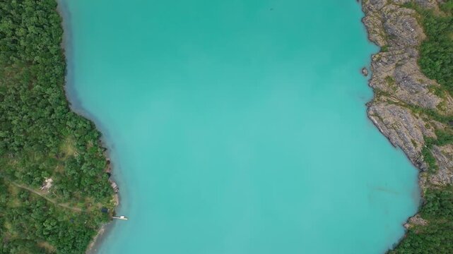 Top-down aerial view of Lovatnet turquoise lake in Norway. Drone reveals milky blue water and natural shoreline patterns in a pristine alpine setting.