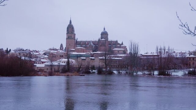 Snowy salamanca cathedral reflecting in the tormes river