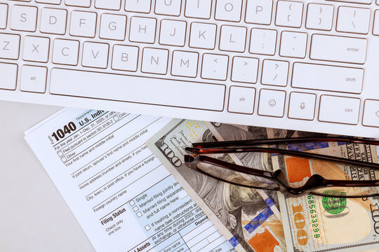 Accouter fills out tax 1040 forms with USA cash, glasses on desk while working computer during tax season