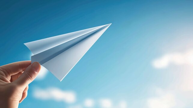 Hand holding a white paper plane against a blue sky