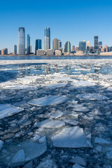 Frozen Hudson River with drifting ice floes and the skyline of downtown Jersey City, New Jersey,...