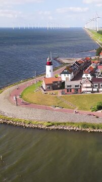 iconic white red topped lighthouse stands grassy point overlooking ijsselmeer gabled houses offshore wind turbines border village urk netherlands structure nautical navigation 