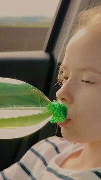 Girl drinking water in the car, Child hydration during a road trip, Thirsty girl with a bottle, Summer travel hydration, Kid quenches thirst in vehicle, Healthy drinking habits for kids, Road journey