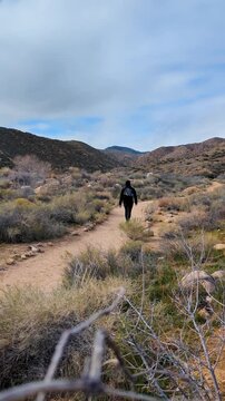 Man walking and hiking on a dirt path trail in the desert of california with mountains