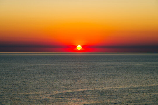 the orange sun sets over the horizon over a calm sea