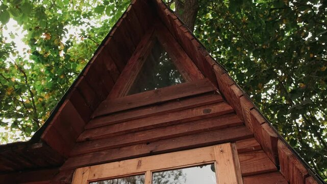 Wooden Cabin Gable Under Leafy Canopy, Angled Upward Shot Of Triangular Window And Cedar Siding, Warm Tones And Dappled Sunlight