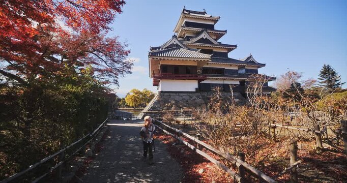 Little boy walking away alone from 16th century Matsumoto castle on autumn path