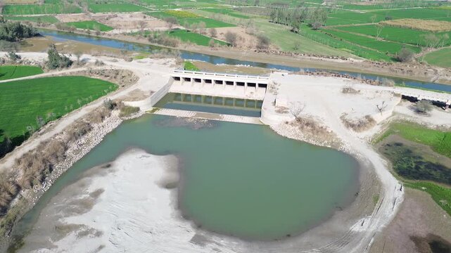 Aerial drone view of a small water barrage and irrigation canal in rural farmland