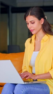Latin hispanic female marketing manager, professional developer specialist working, browsing laptop computer sitting on sofa in office coworking. Young woman employee using pc for business. Vertical