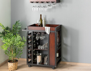 Industrial-inspired rolling bar cart with dark wood panels, metal frame, integrated wine rack, suspended glass hangers, a refined modern entertaining vibe, beautifully enhanced by lush indoor greenery © Jesus