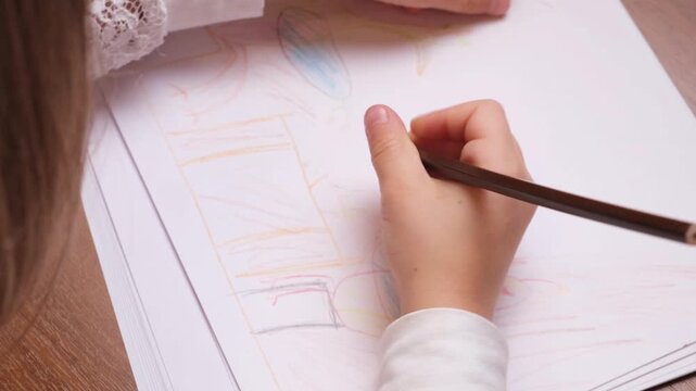 Close view of a young child drawing with a pencil on a sheet of paper, simple home or classroom scene showing concentration, creativity and early learning through art.
