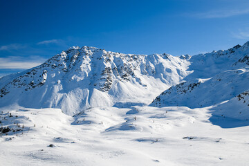 Snow-covered alpine mountains under a clear blue sky, pristine winter landscape with soft light and wide open space, calm and majestic natural scenery.