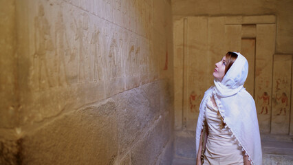 A woman exploring an ancient Egyptian temple, admiring historic wall carvings while enjoying a cultural vacation and travel experience.
