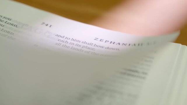 Bible Zephaniah book pages turn during a close up study of holy scripture. A detailed shot of flipping white paper in the Old Testament prophetic book about judgment and restoration in a study.