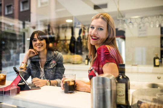 Young people in their twenties look at a tablet inside a bar while having drinks.