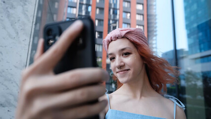A teenage girl poses and smiles for a selfie on a smartphone.