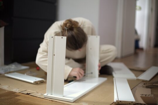 Woman assembling flat pack furniture at home. Female person building cabinet using tools and instruction manual.