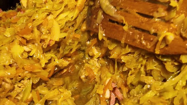 Preparing of traditional dish bigos with sausage, meat, carrot and cabbage on a frying pan, stewed cabbage. 