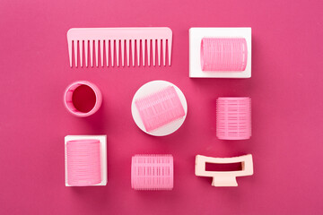 Pink hair curlers on color background, top view