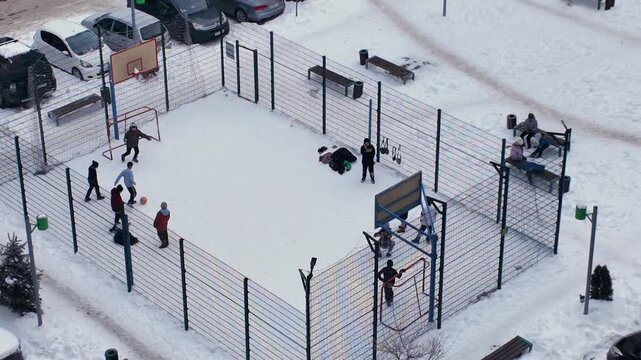 Snowfall in the city. Teenagers play soccer on a sports yard of a residential complex on a snowy winter day