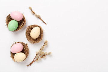 Colorful easter eggs in nests with flowers on color background, top view