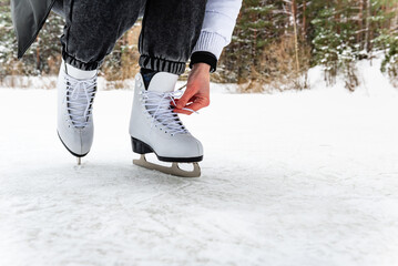 Close-up of a woman lacing white figure skates, preparing to skate on a frozen outdoor rink in winter.
