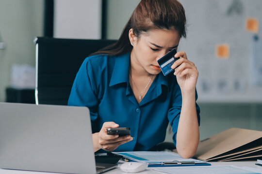 Young businesswoman is holding two credit cards with a worried expression, trying to decide which one to use to pay off her debt