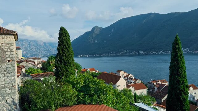 Montenegro, picturesque scenery of seaside promenade on a sunny day, moored boats, brick-colored tiled roofs, a mountain range in the background