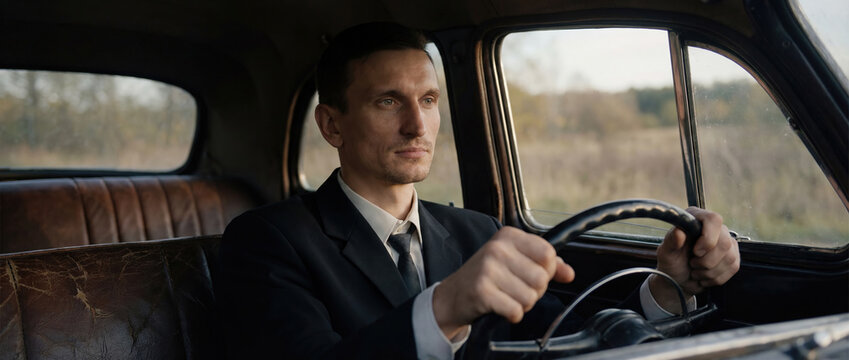 Man driving vintage car on forest road in rainy evening
