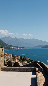 Montenegro, picturesque scenery of seaside promenade on a sunny day, moored boats, brick-colored tiled roofs, a mountain range in the background