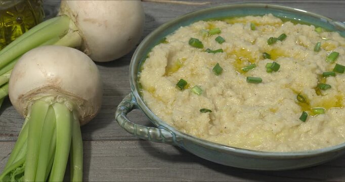 Turnip Skordalia. Creamy Greek dip made of turnips, garlic, and olive oil. Two whole turnips next to a bowl with dip garnished with olive oil and chopped scalions. 