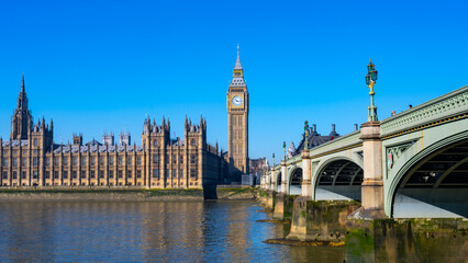 Fototapeta premium The Houses of Parliament and Big Ben above the River Thames in London. The sky is clear and the iconic landmarks stand tall and proud.